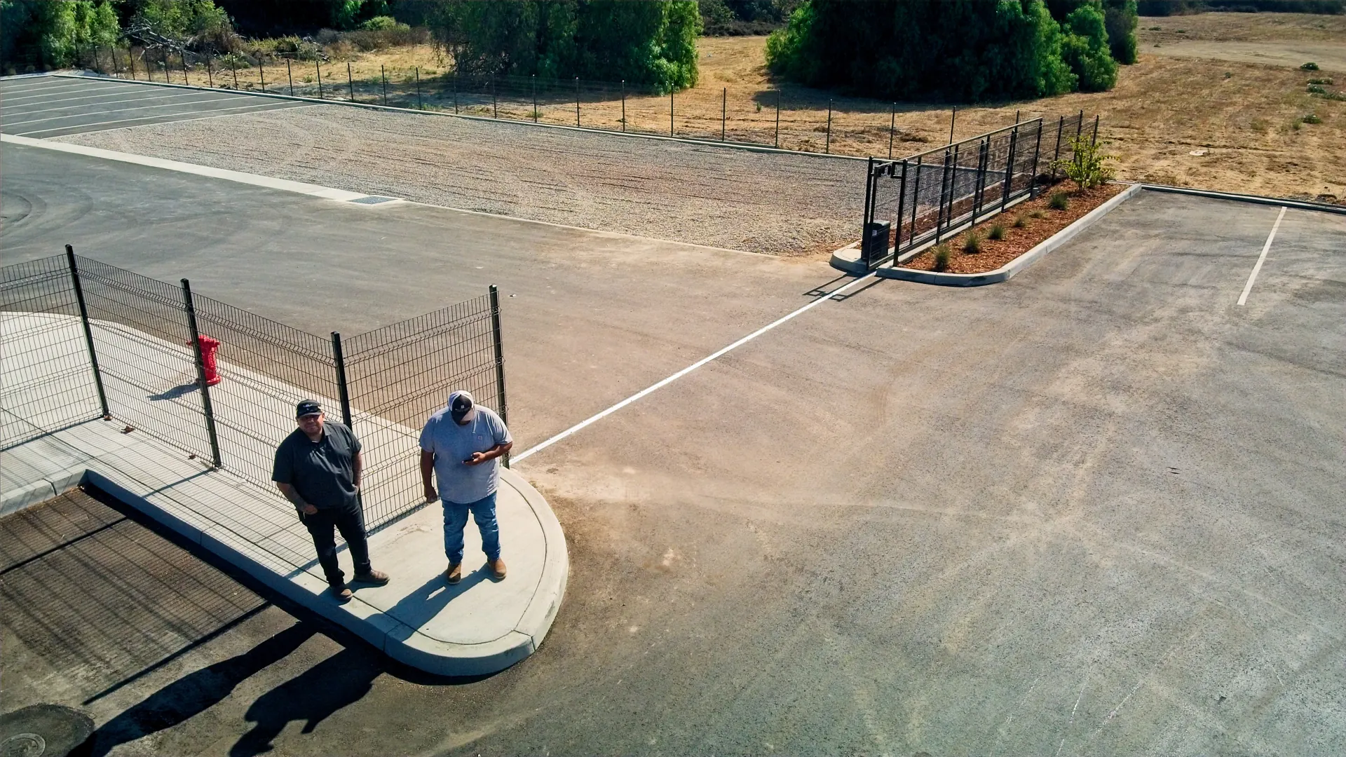 Aerial view of two people inspecting a finished steel fence line and rolling gate